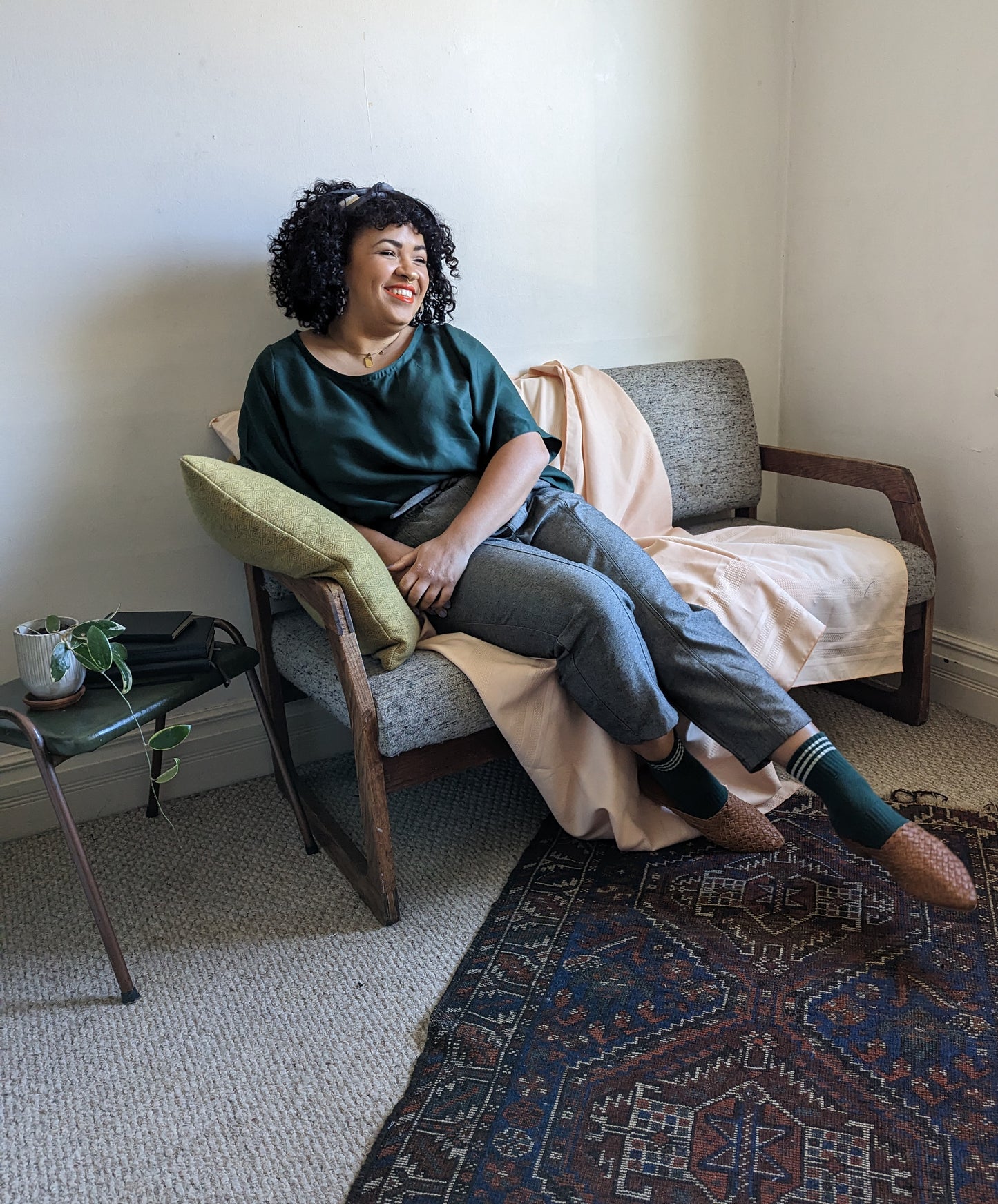 Our model Ali wears this gender neutral T shirt in Phthalo Green, paired with raw denim trousers in Pebble while seated.