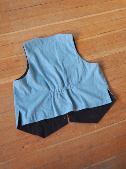 A light blue sleeveless vest with a black inner lining and hem, laid flat on a wooden floor.