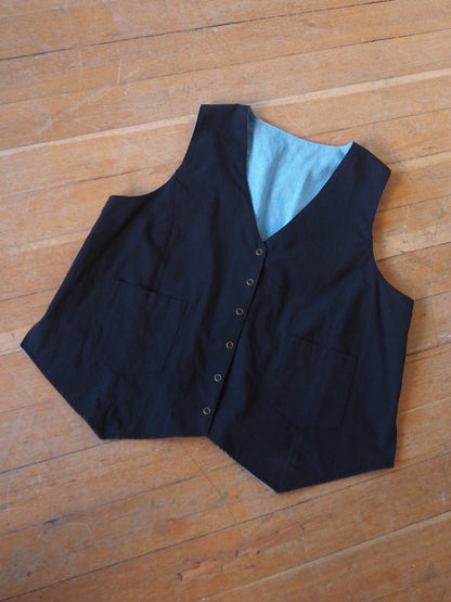 A black waistcoat vest with a light blue lining, laid flat on a wooden floor.