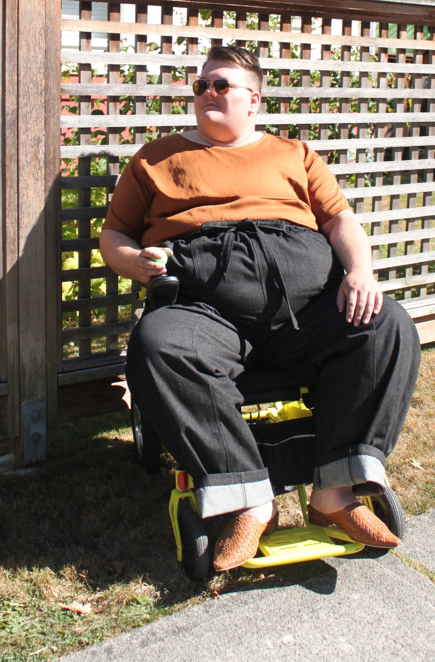 Robin Roscoe models the Cedar gender neutral T shirt tucked into a pair of raw denim trousers while seated.